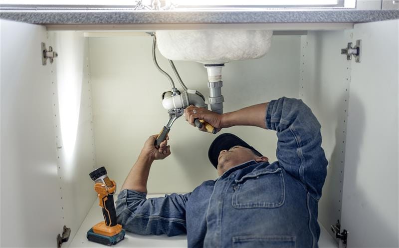 Plumber repairing pipes beneath a bathroom sink in El Dorado Hills